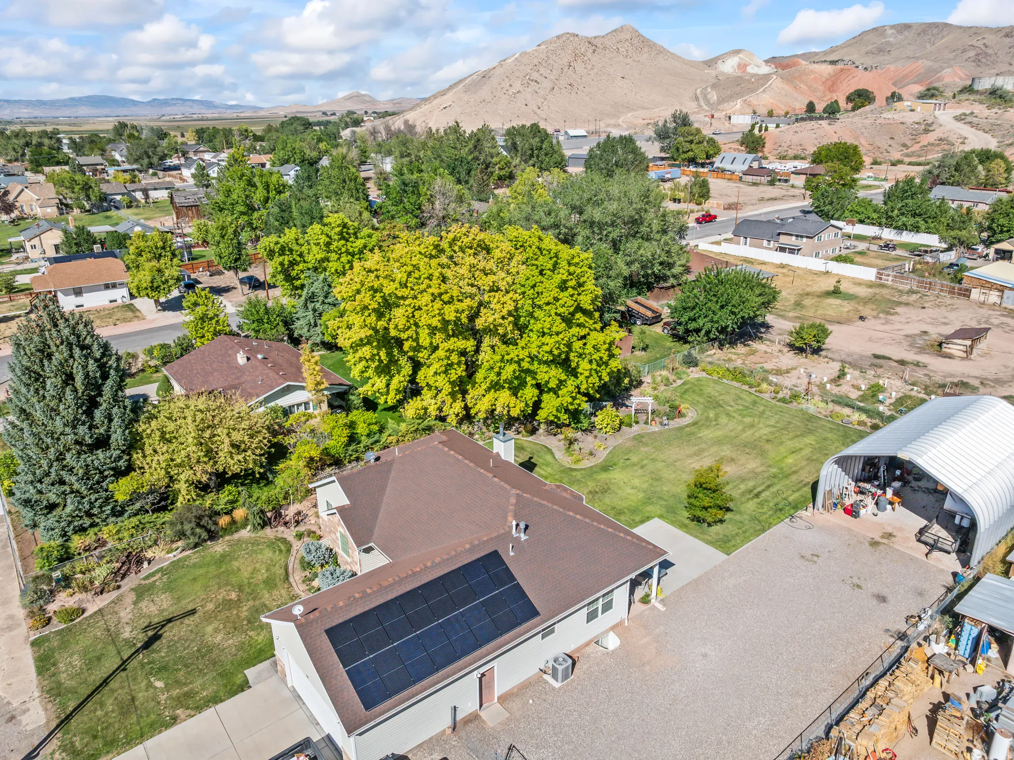 Solar panel array on the roof, expansive paved driveway, detached arch-style metal structure, manicured lawn, and mature trees