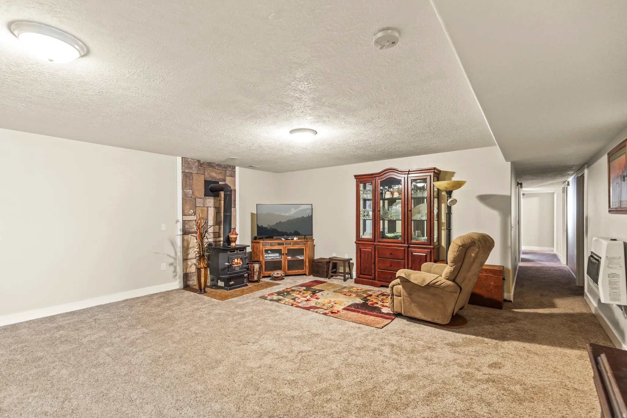 Carpeted room featuring a stone accent wall, a black wood-burning stove, and flush-mount ceiling lighting