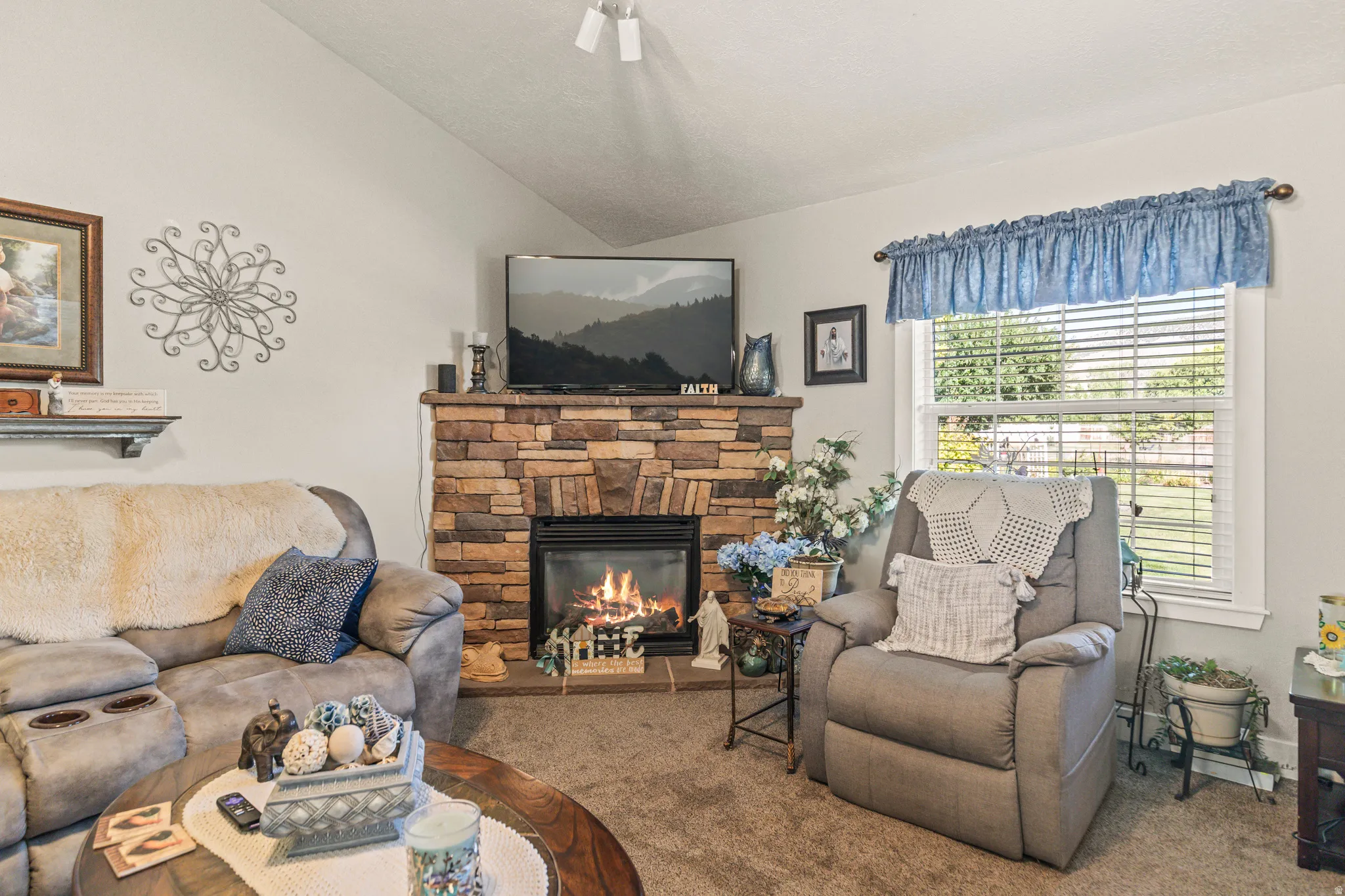 Stone-clad corner fireplace with a hearth, white window trim, and track lighting