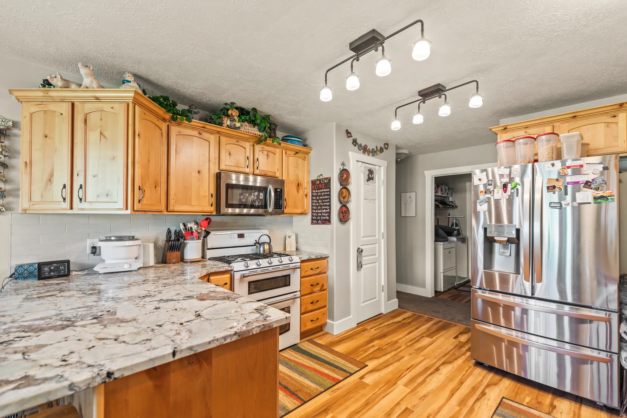 Wood-finish flooring, stainless steel appliances, light wood cabinetry, white subway tile backsplash, and light-toned countertops