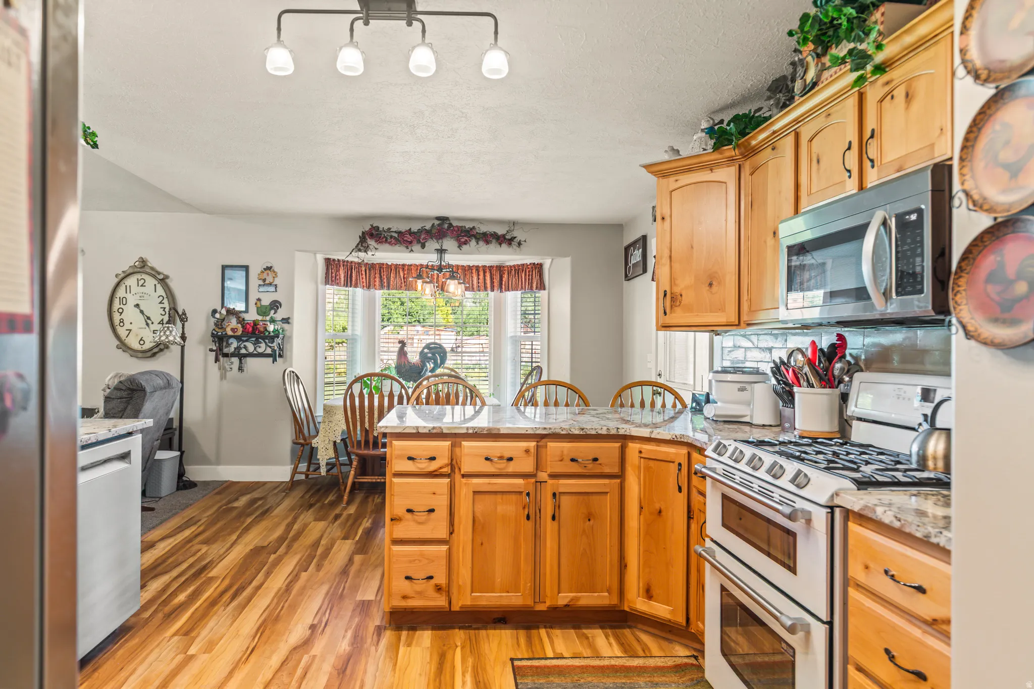Kitchen featuring wood-finish flooring, light wood cabinetry, stone countertops, stainless steel appliances, and a central island with seating
