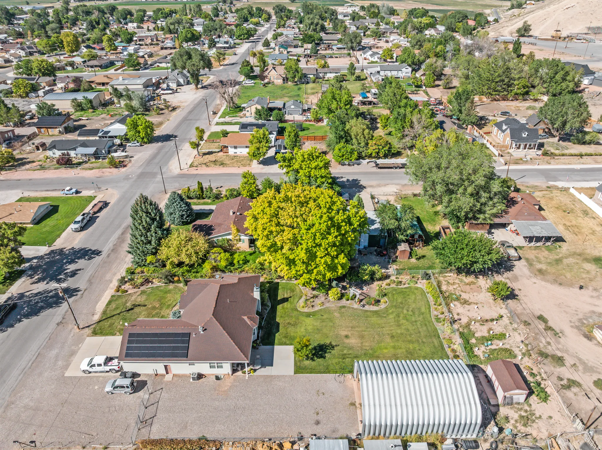 Property featuring a brown shingle roof with solar panels, a detached metal Quonset hut, and a separate storage shed