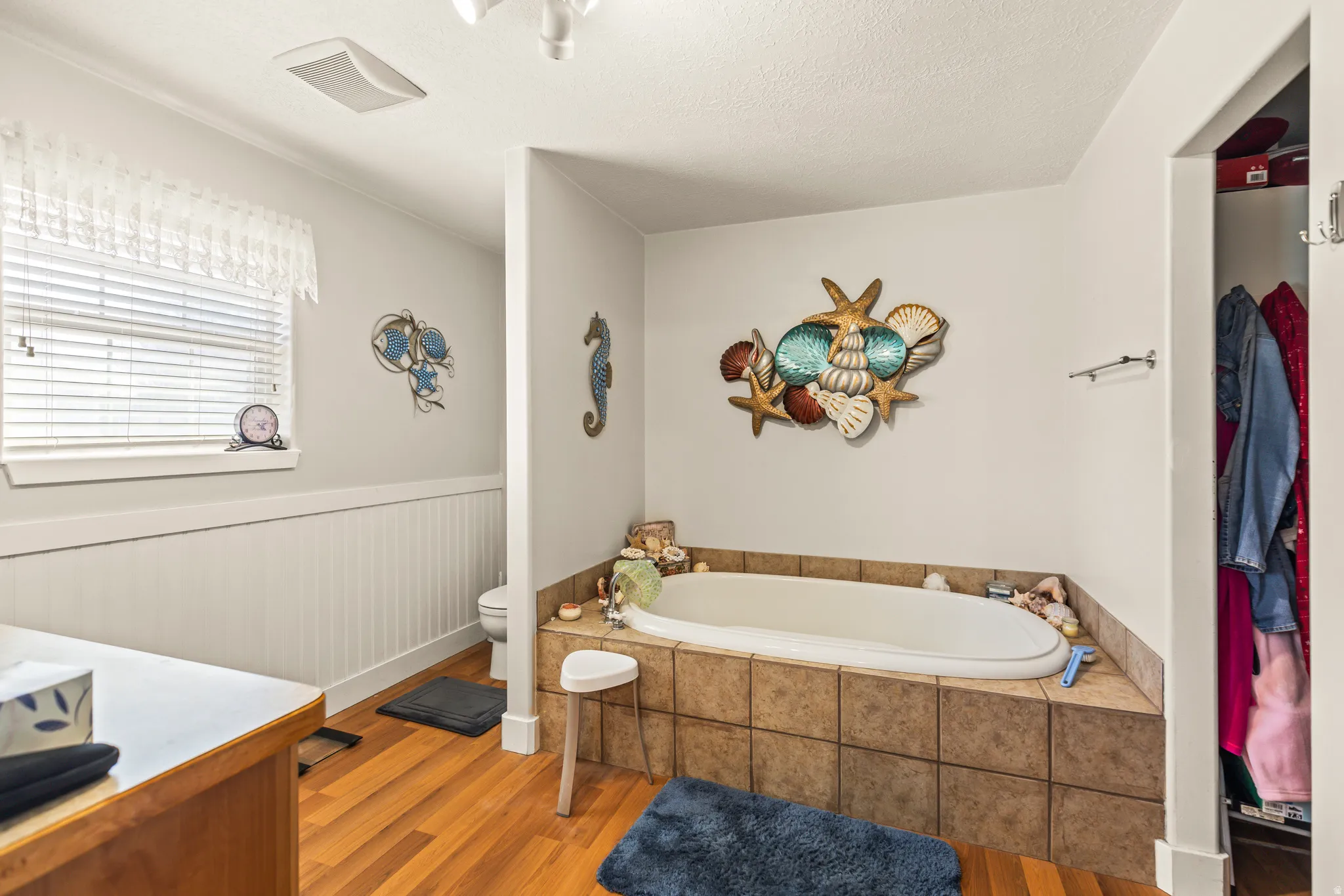 Built-in soaking tub with tile surround, wood-finish flooring, and a window with blinds