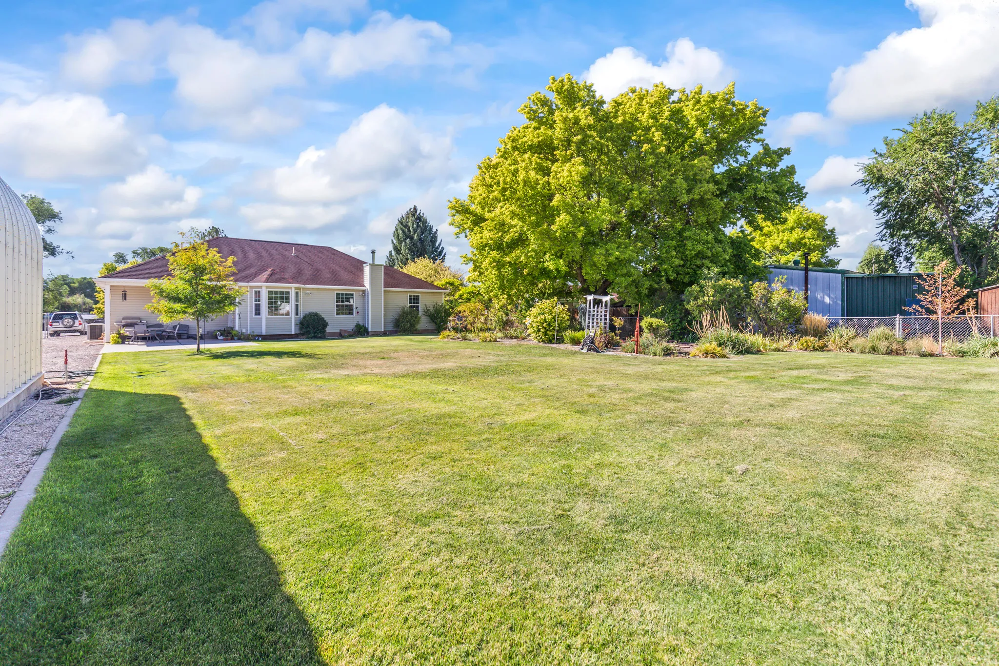 Expansive lawn area, mature trees, single-story residence with a covered patio, and gravel driveway