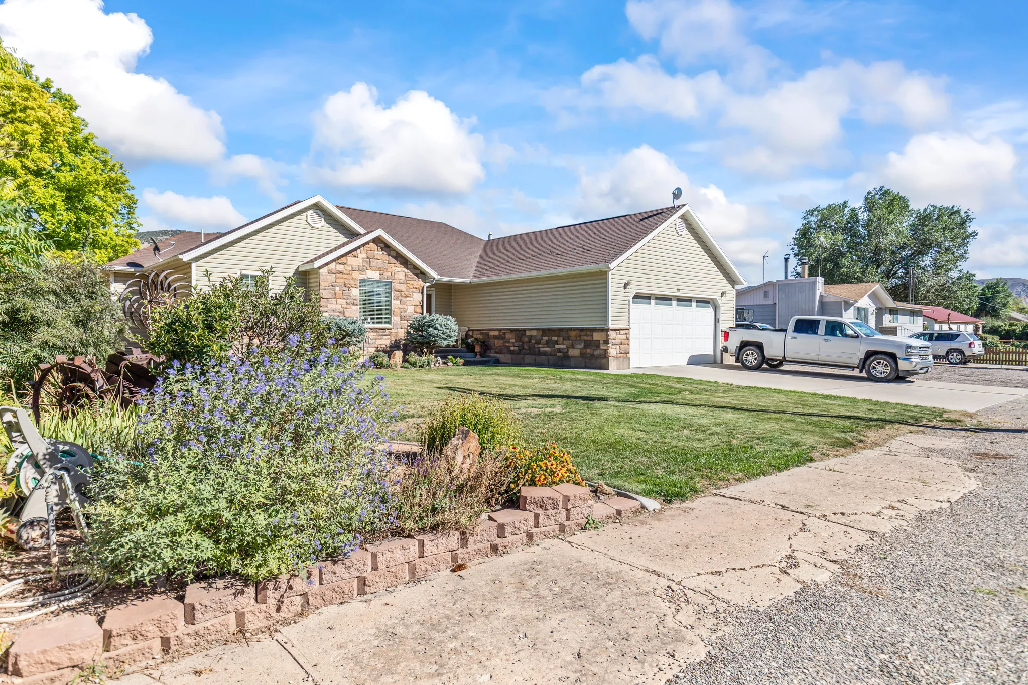 Exterior featuring stone and siding finishes, an attached garage, a manicured lawn, and mature landscaping