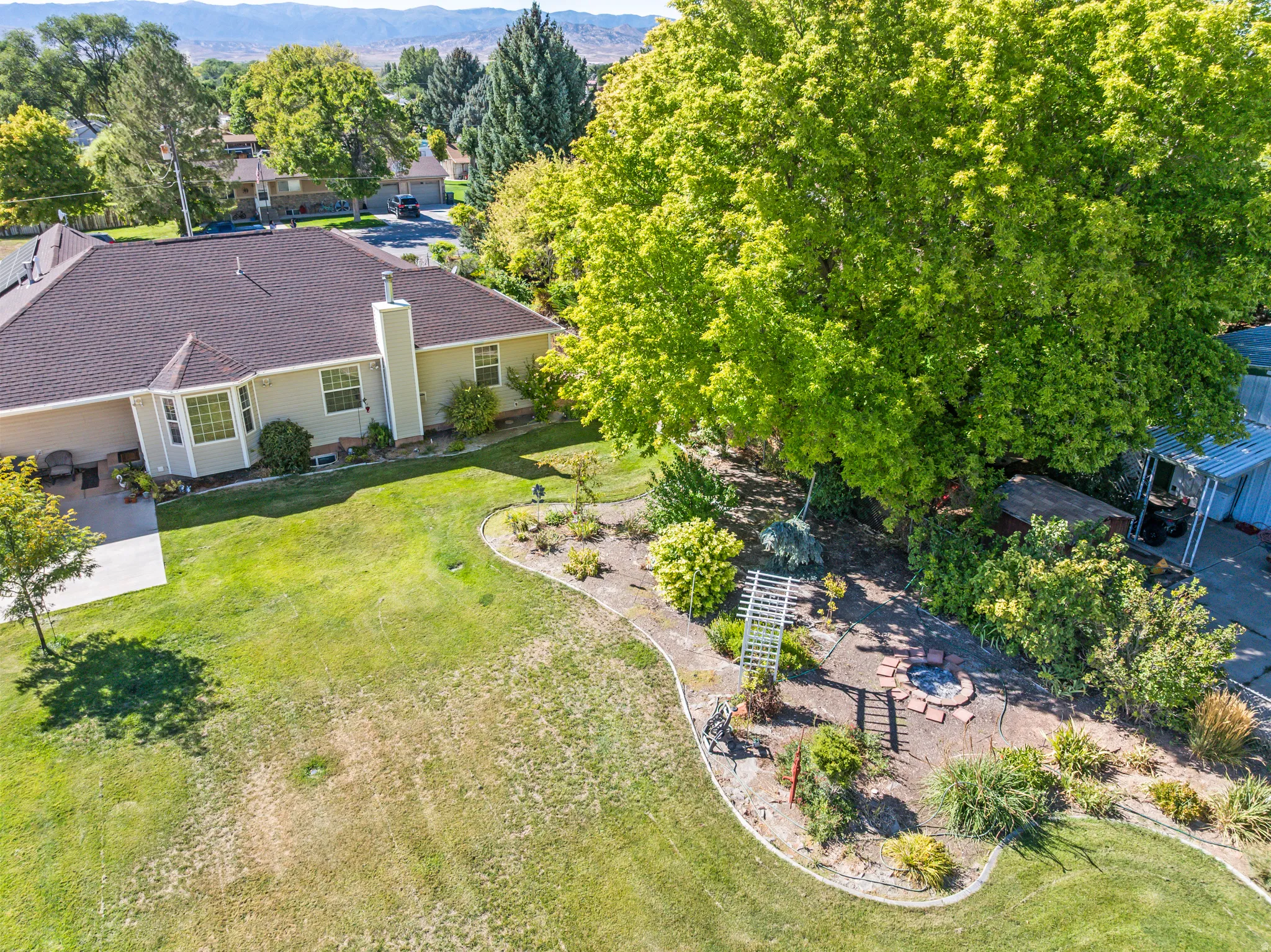 Expansive green lawn with mature trees, a dedicated fire pit area, and landscaped garden beds