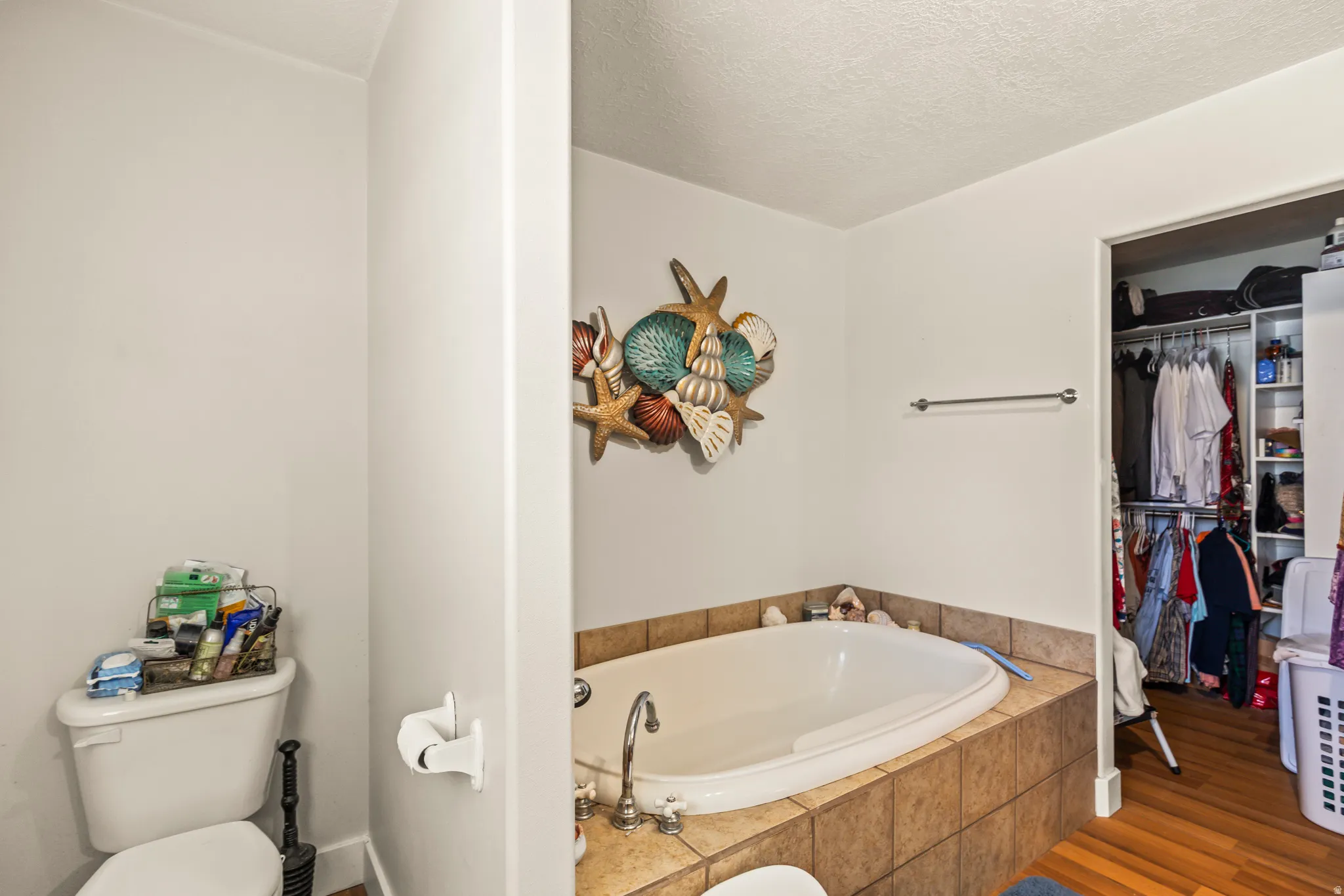 Built-in soaking tub with tile surround, white walls, and an open closet with built-in shelving