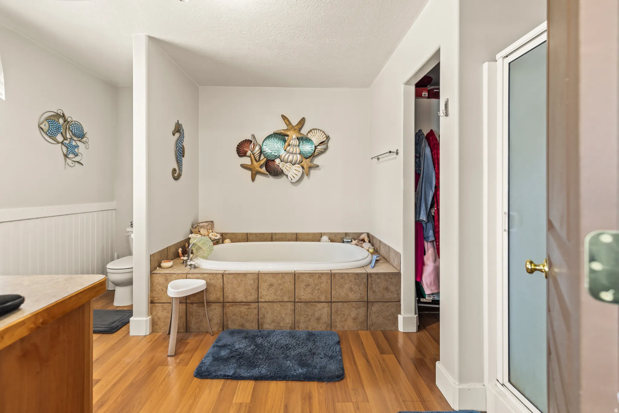 Built-in soaking tub with tile surround, wood-finish flooring, and white wall paneling