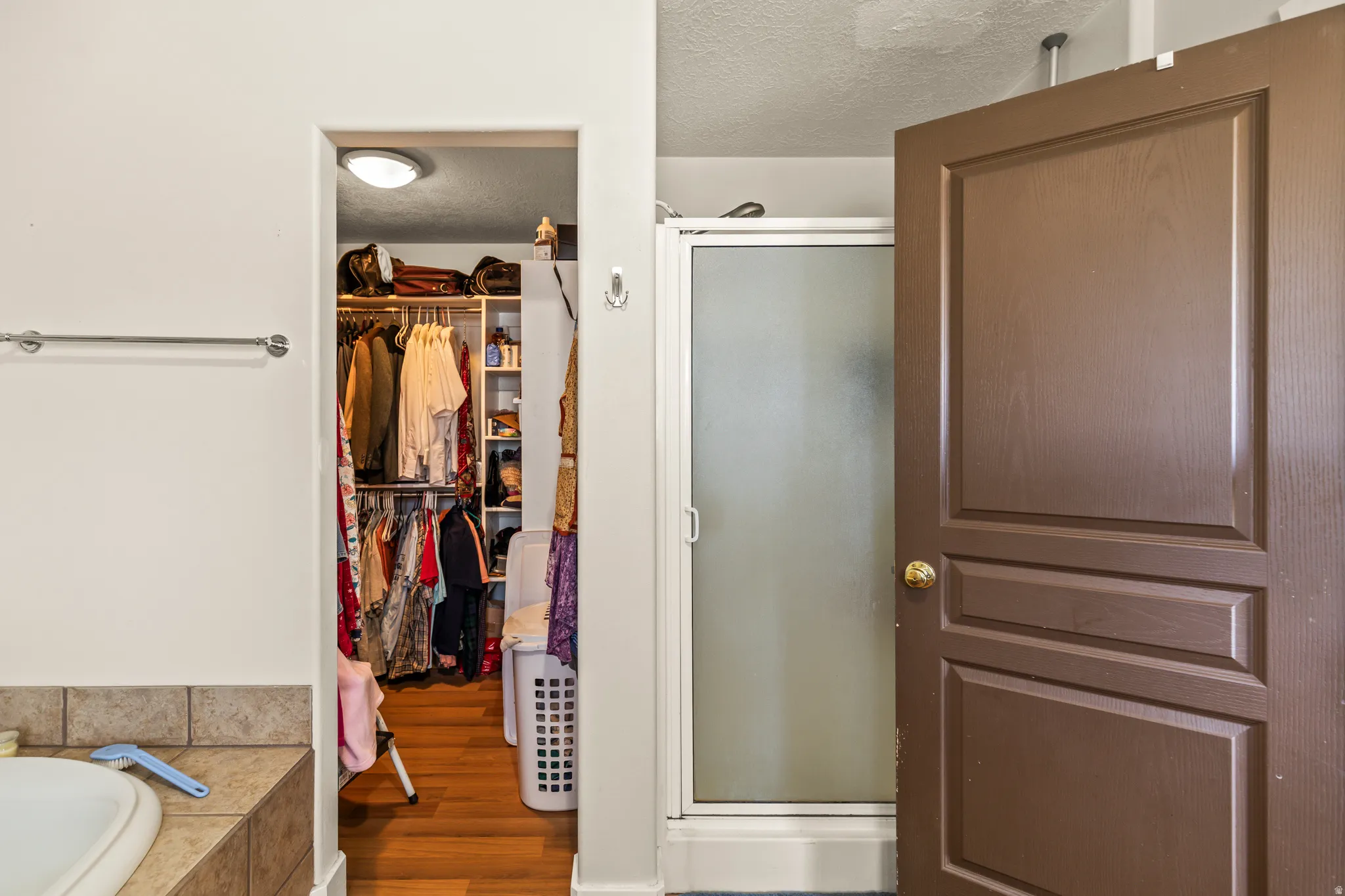 Walk-in closet with wood-finish flooring and recessed lighting, adjacent to a shower enclosure with frosted glass