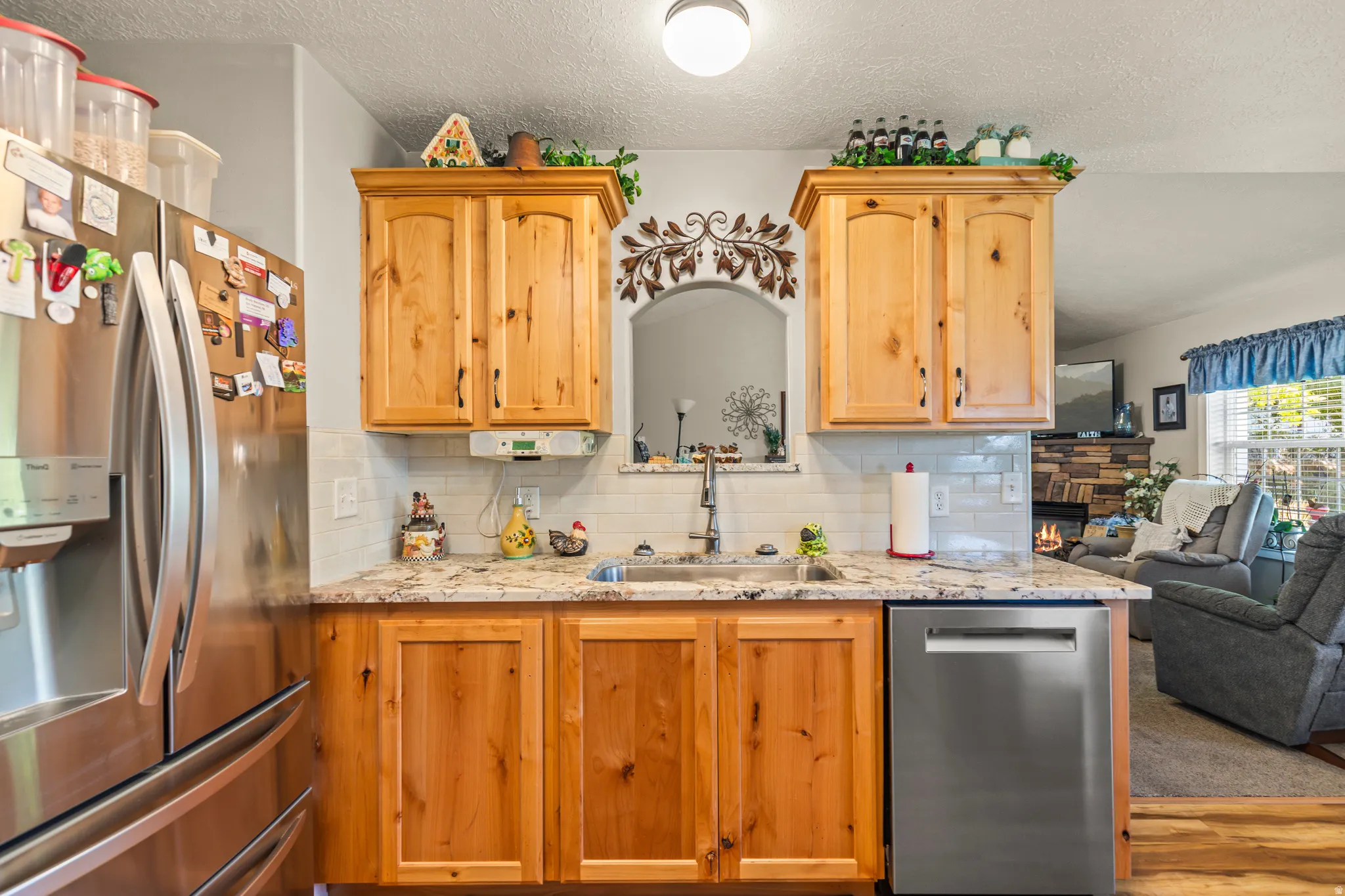 Stainless steel French door refrigerator, wood-finish cabinetry, granite-style countertops, subway tile backsplash, and a stainless steel dishwasher