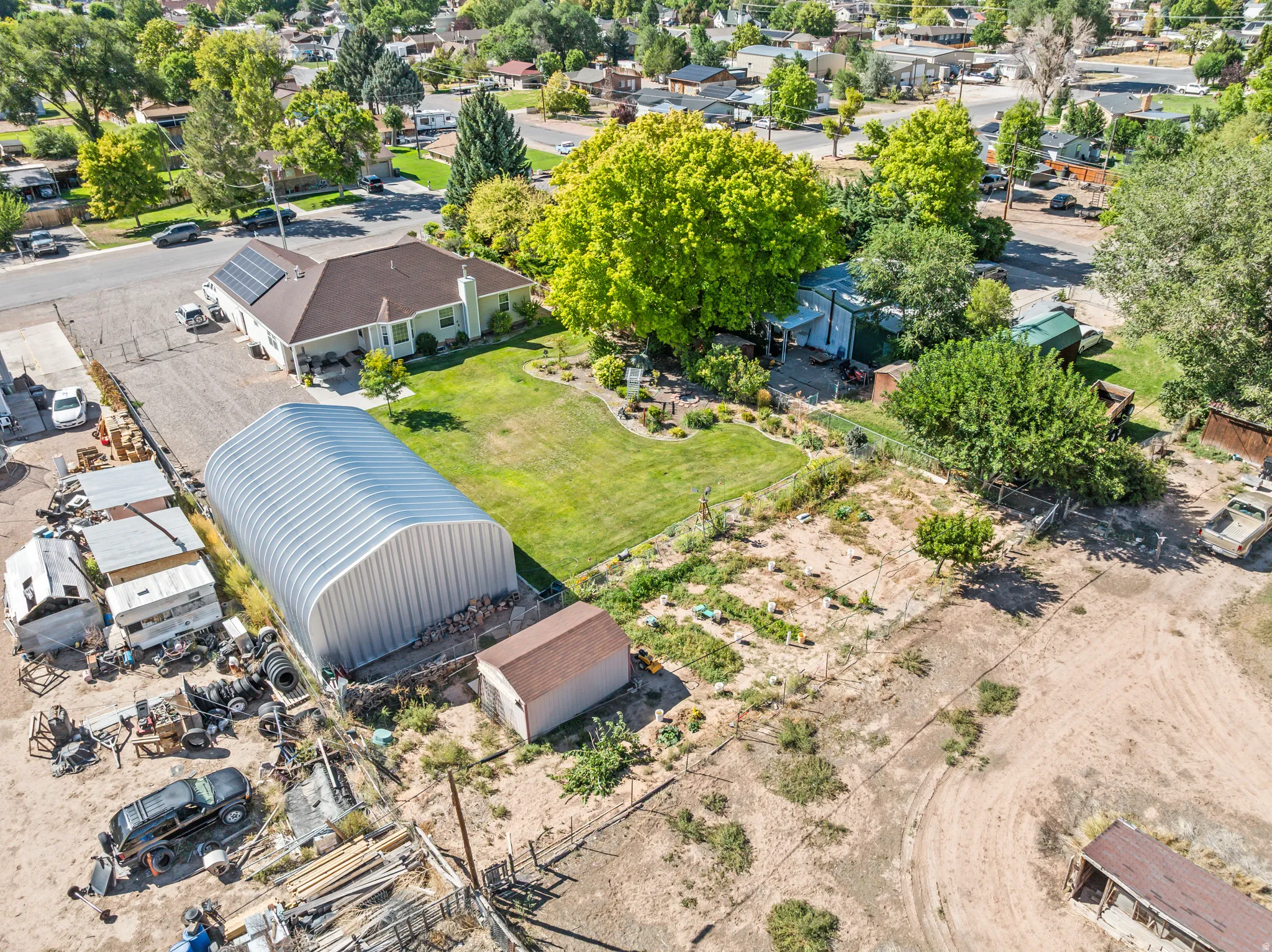 Ranch-style residence featuring solar panels, a substantial metal Quonset hut, a separate storage shed, a manicured lawn, and mature trees