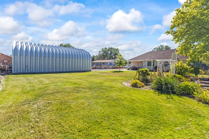 Expansive grassy area featuring a large arched metal outbuilding and a landscaped garden bed