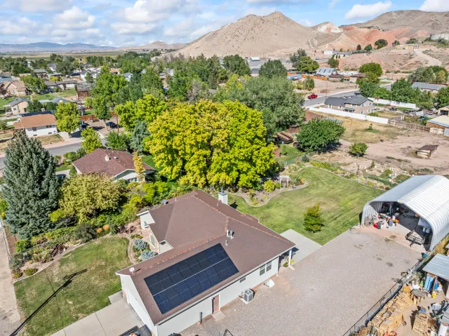 Solar panel array on the roof, expansive paved driveway, detached arch-style metal structure, manicured lawn, and mature trees