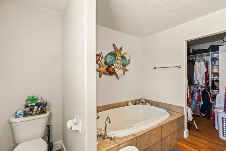 Built-in soaking tub with tile surround, white walls, and an open closet with built-in shelving