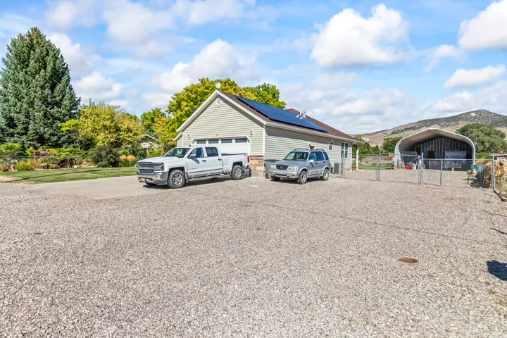 Exterior featuring light-colored siding, a two-car garage, roof-mounted solar panels, a gravel driveway, and a metal-frame utility structure