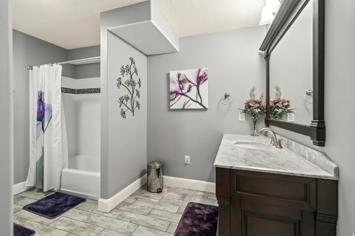Wood-finish plank flooring, single vanity with integrated sink, stone countertop, built-in tub with tile surround, and an ornate framed mirror
