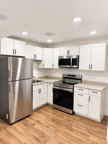 White shaker cabinetry with matte black hardware, light-toned countertops, stainless steel appliances, and wood-finish flooring