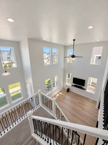 Two-story living area with high ceilings, multiple windows, wood-finish flooring, recessed lighting, and a ceiling fan