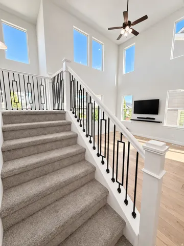 Two-story great room featuring high ceilings, multiple large windows, a ceiling fan, and wood-finish flooring