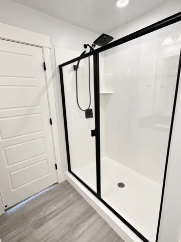 Shower enclosure with clear glass panels and matte black framing, featuring a dual-head shower system and integrated shelving