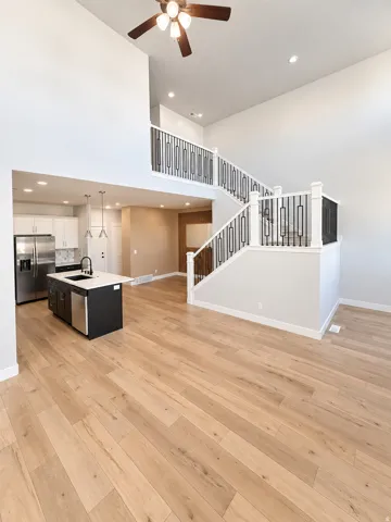Vaulted ceiling with a ceiling fan, wood-finish flooring, and a contemporary staircase with metal balusters