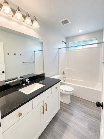 White vanity with gold-tone hardware, black countertop, undermount sink, and wood-finish flooring