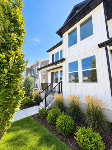 White exterior with black trim, board and batten siding, multiple large windows, a covered entry, and a manicured lawn with landscaping