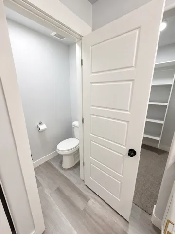 White paneled door with matte black hardware, wood-finish flooring, and a white toilet
