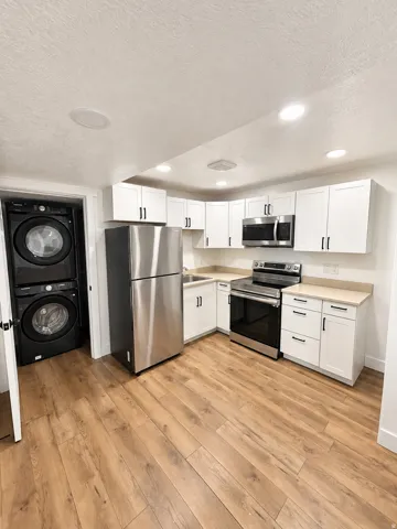 Modern kitchen featuring white shaker cabinetry, stainless steel appliances, wood-finish flooring, and recessed lighting