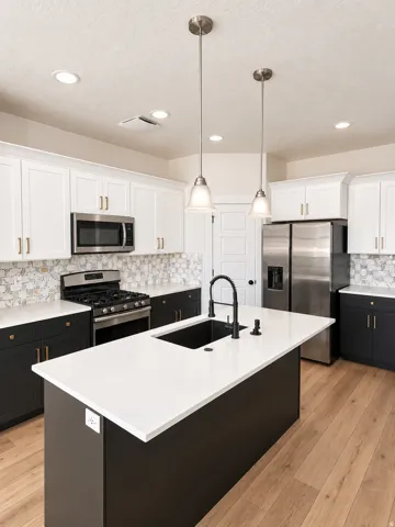 Kitchen featuring a large island with an undermount sink, stainless steel appliances, white and dark cabinetry, a decorative tile backsplash, and light wood-finish flooring