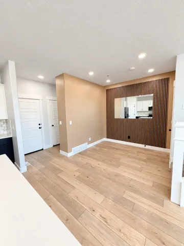 Recessed lighting, light wood-finish flooring, accent wall with vertical wood paneling, white baseboards, and a built-in mirror