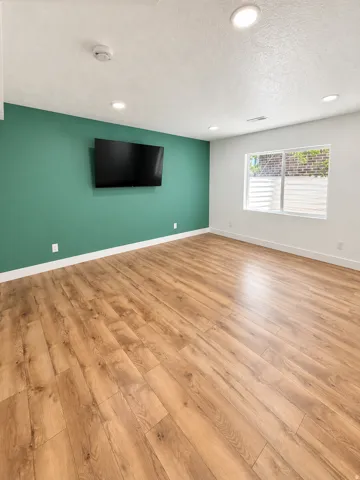Recessed ceiling lighting, wood-finish flooring, accent wall, and a window with blinds