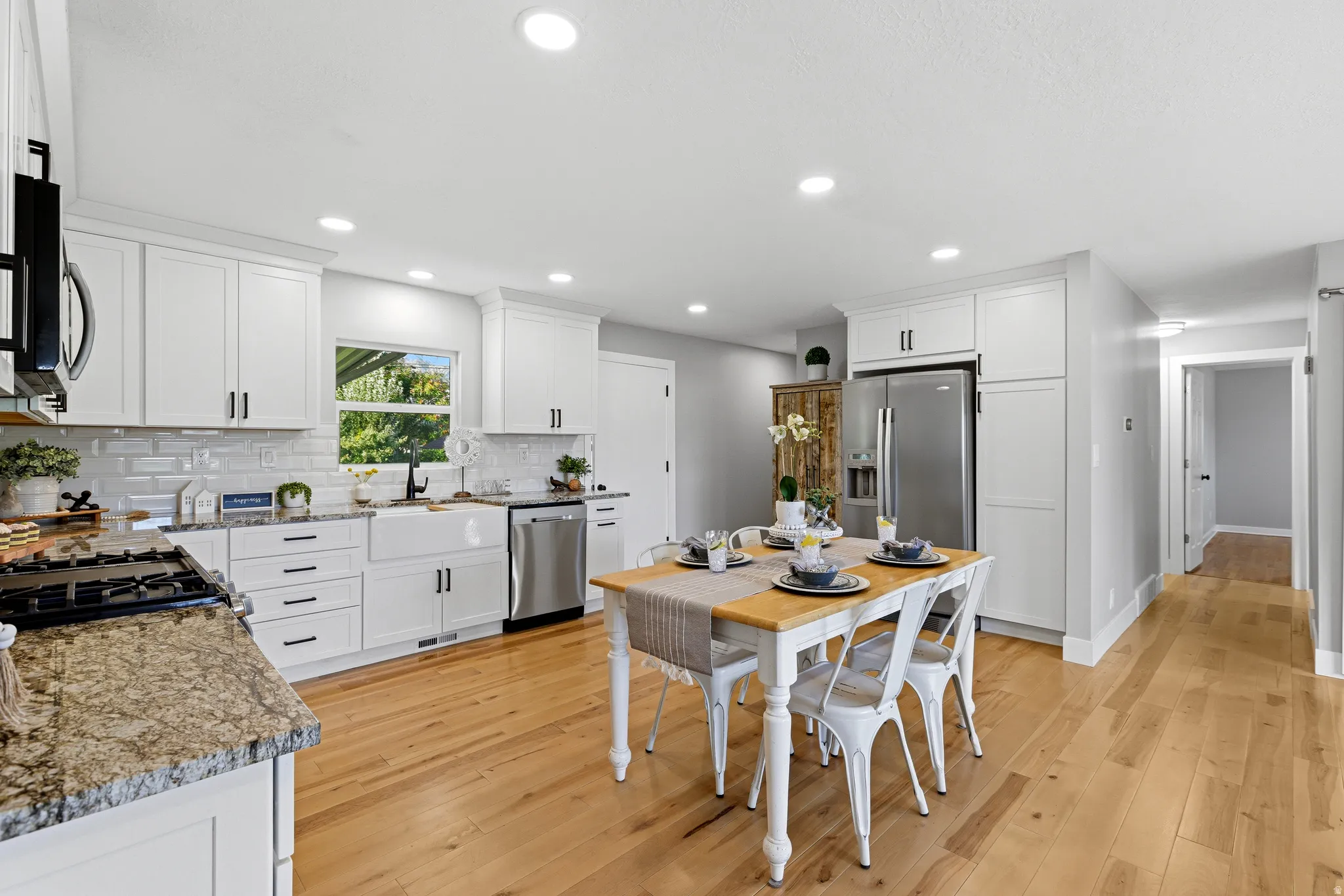 Open white farmhouse style kitchen with hardwood floors, apron sink and stainless steel appliances
