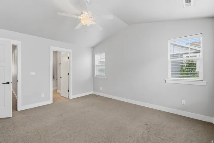 Vaulted ceiling with a ceiling fan, light gray wall paint, two pane windows with blinds, and neutral carpet flooring