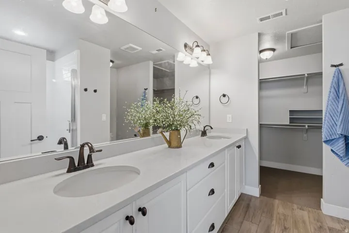 Dual vanity with integrated sinks, white cabinetry, quartz-finish countertop, dark bronze fixtures, and wood-finish flooring