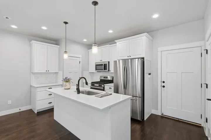 Kitchen featuring an island with a sink, white cabinetry, stainless steel appliances, dark wood-finish flooring, and pendant lighting
