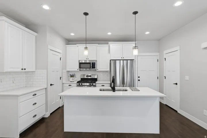 Kitchen featuring white shaker cabinetry, stainless steel appliances, a center island with sink, subway tile backsplash, and dark wood-finish flooring