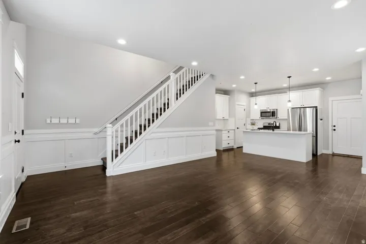 Hardwood flooring, white wainscoting, white kitchen cabinetry, stainless steel appliances, and recessed lighting