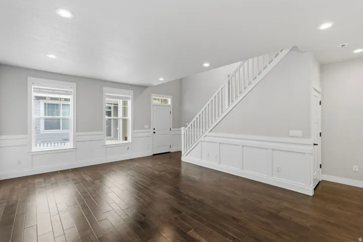 Wood-finish flooring, recessed lighting, white wainscoting, white window trim, and a white staircase with balusters