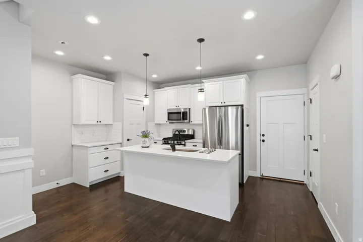 Kitchen featuring white cabinetry, stainless steel appliances, a center island with a white countertop, dark wood-finish flooring, and recessed lighting