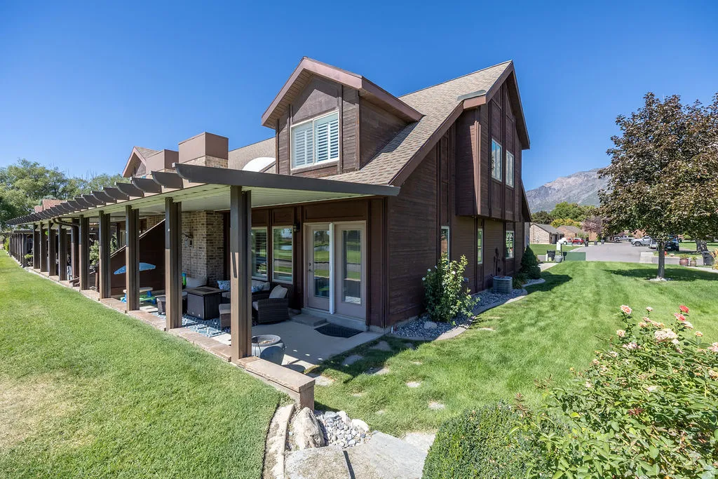 Expansive green space with an extended covered patio featuring a slatted roof, brick exterior accents, and dual glass pane doors