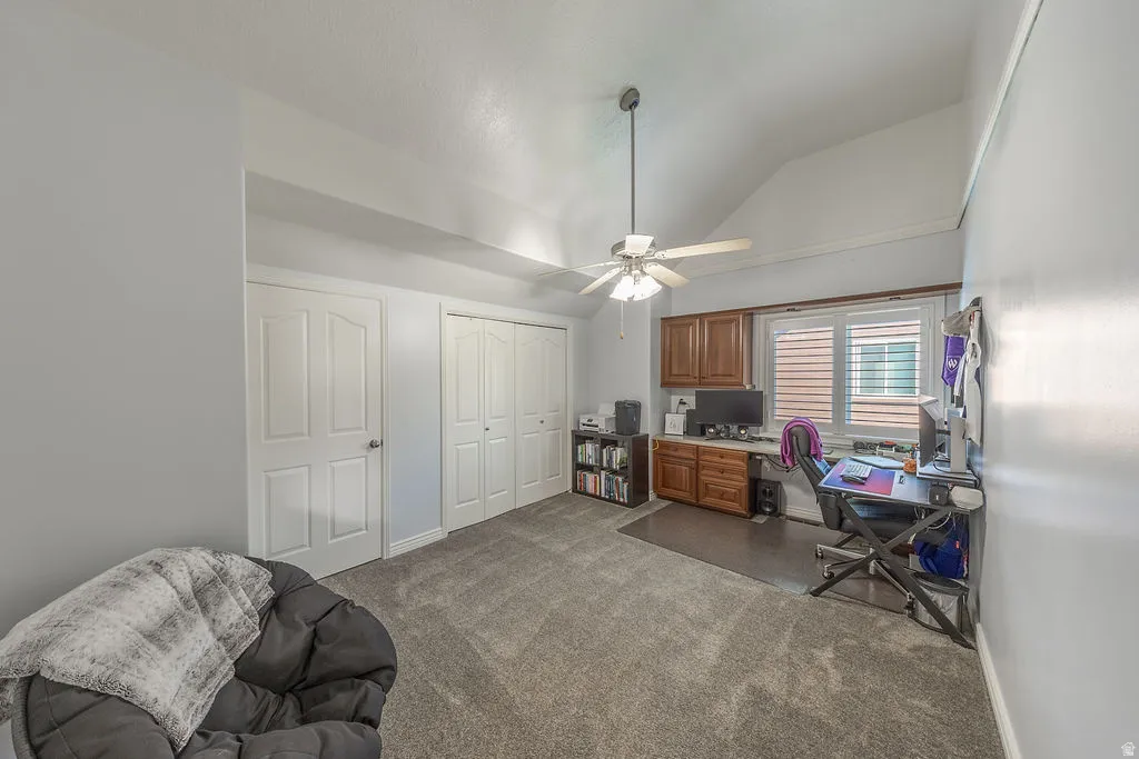 Vaulted ceiling, ceiling fan with light, built-in wooden cabinetry, window with plantation shutters, and light grey carpeting
