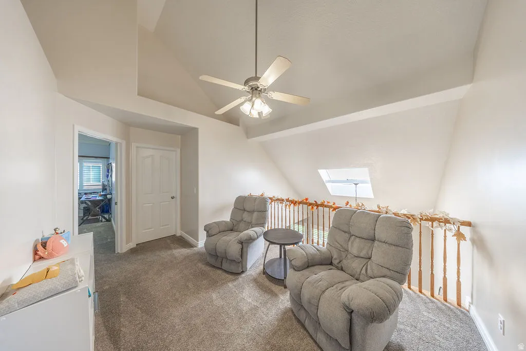 Carpeted loft space featuring an angled ceiling, ceiling fan with light fixture, and a skylight