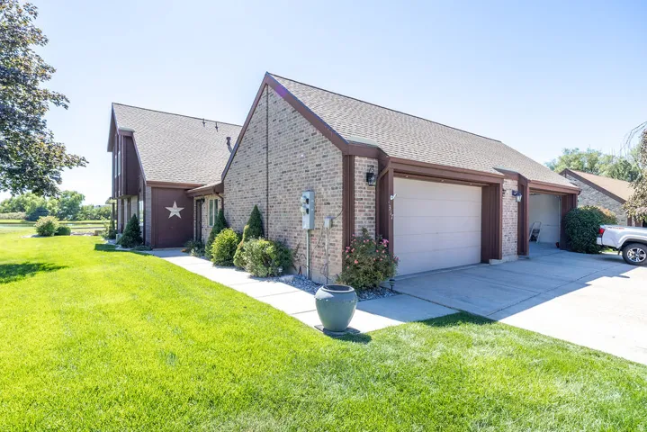Brick exterior with a multi-car garage, mature landscaping, and a concrete driveway