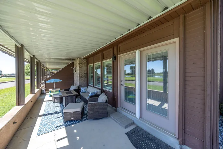 Covered patio with concrete flooring, support columns, exterior wood siding, and brick accents