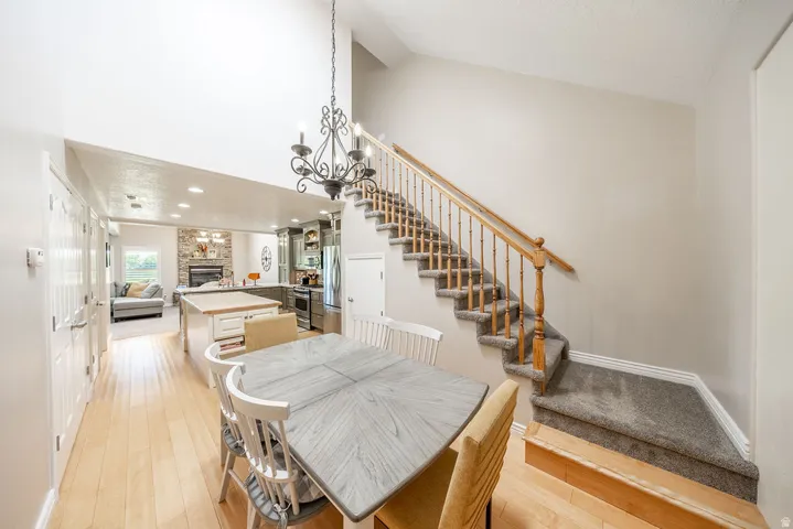 Spacious open-concept interior with vaulted ceilings, light wood-finish flooring, a grand staircase with wood railing, and a stone-faced fireplace