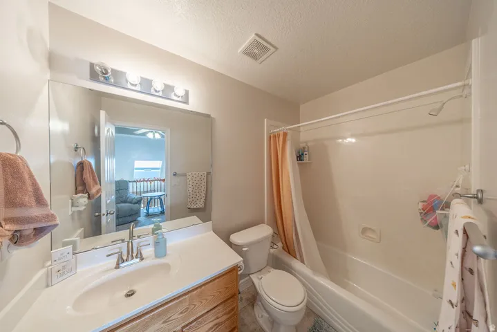 Bathroom featuring a single vanity, wood-finish cabinetry, a large wall-mounted mirror, a four-bulb vanity light fixture, and a combination bathtub and shower with a showerhead
