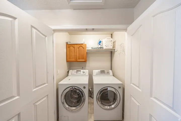 Laundry closet with dual front-load appliances, built-in shelving, and wood-finish cabinetry