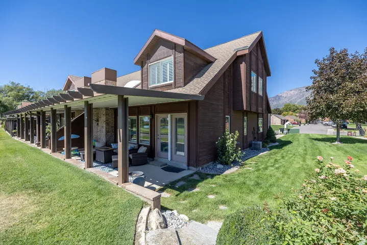 Expansive green space with an extended covered patio featuring a slatted roof, brick exterior accents, and dual glass pane doors