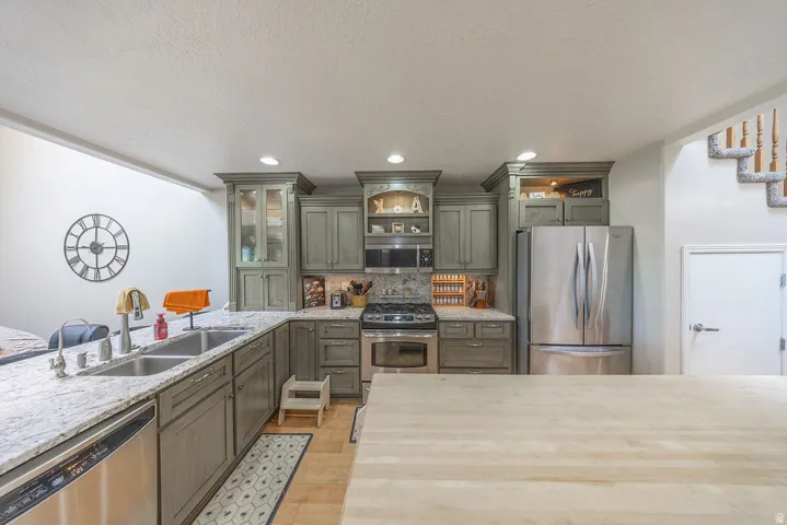 Kitchen featuring granite countertops, stainless steel appliances, custom cabinetry, recessed lighting, and a double basin sink